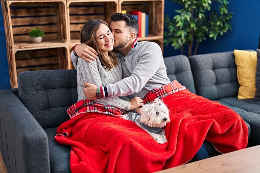 Man and woman hugging and kissing sitting on sofa with dog at home