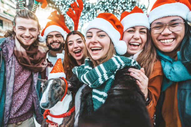 Self portrait of mixed race young people wearing santa claus hat celebrating Christmas day outside - Happy multiracial friends group taking selfie having xmas holiday party - Winter holidays concept stock photo