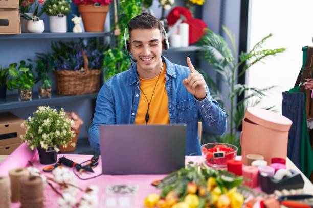 bel homme hispanique travaillant chez un fleuriste faisant un appel vidéo souriant avec une idée ou une question pointant du doigt avec un visage heureux, numéro un - gardening humor meeting conference call photos et images de collection