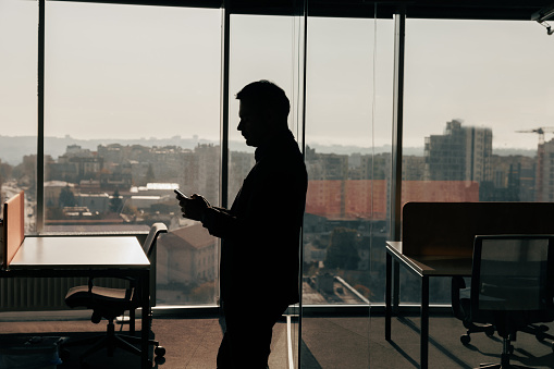 Silhouette of a businessman with phone in his hands standing in office. High quality photo