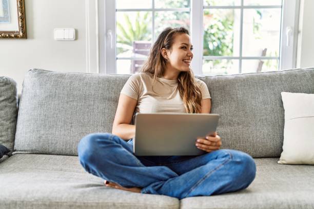 istock Young hispanic girl using laptop sitting on the sofa at home. 1437869350