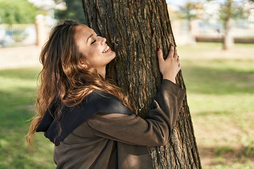 Young beautiful hispanic woman smiling confident hugging tree at park