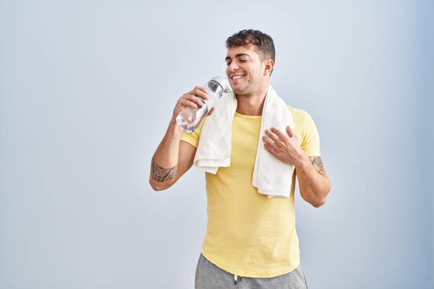 Young hispanic man drinking water standing at sport center
