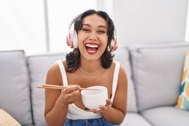 Young hispanic woman eating asian food using chopsticks smiling and laughing hard out loud because funny crazy joke. Young hispanic woman eating asian food using chopsticks smiling and laughing hard out loud because funny crazy joke. people laughing hard stock pictures, royalty-free photos & images
