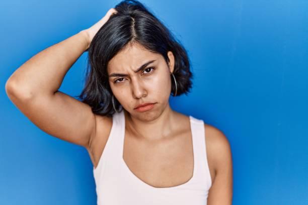 istock Young hispanic woman standing over blue background confuse and wonder about question. uncertain with doubt, thinking with hand on head. pensive concept. 1437871088