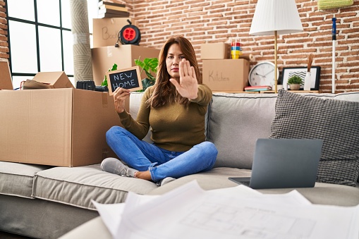 Hispanic woman moving to a new home with open hand doing stop sign with serious and confident expression, defense gesture