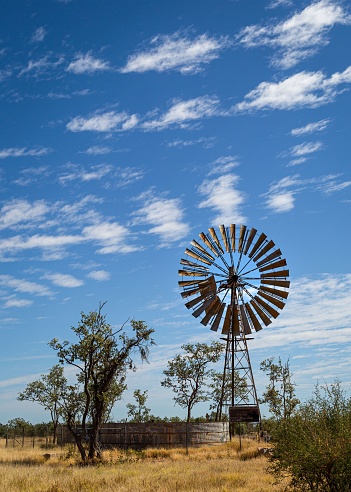 A vertical shot of old wind pump for cattle in outback Queensland, Australia under blue cloudy sky