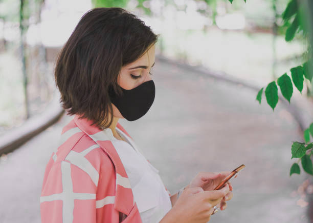 istock Woman looking at her phone and wearing a protective mask 1437875422