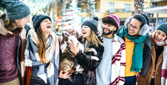 Happy friends group having fun together with cute dog on winter holidays - Life style concept with trendy young people wearing fashion clothes outdoors - Bright azure filter on wide horizontal crop