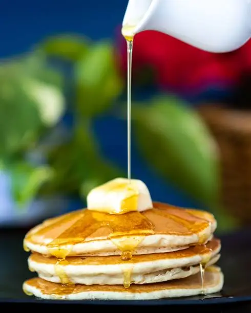 A vertical shot of pouring honey on hotcakes with a butter pat on top