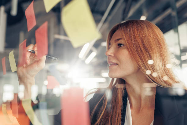 istock Businesswoman writing on sticky notes on glass wall while working in office 1437876091