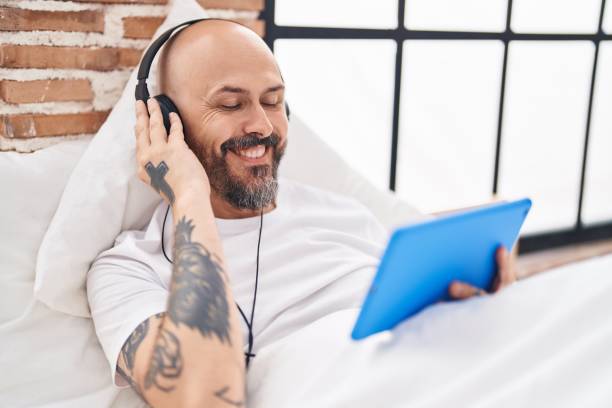 istock Young bald man watching video on touchpad on bed at bedroom 1437878012