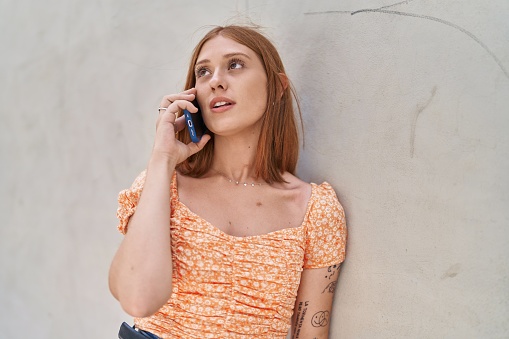 Young redhead woman talking on the smartphone over white isolated background