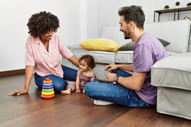 couple et fille souriants confiants jouant avec des jouets assis sur le sol à la maison - spanish culture couple family latin american and hispanic ethnicity photos et images de collection