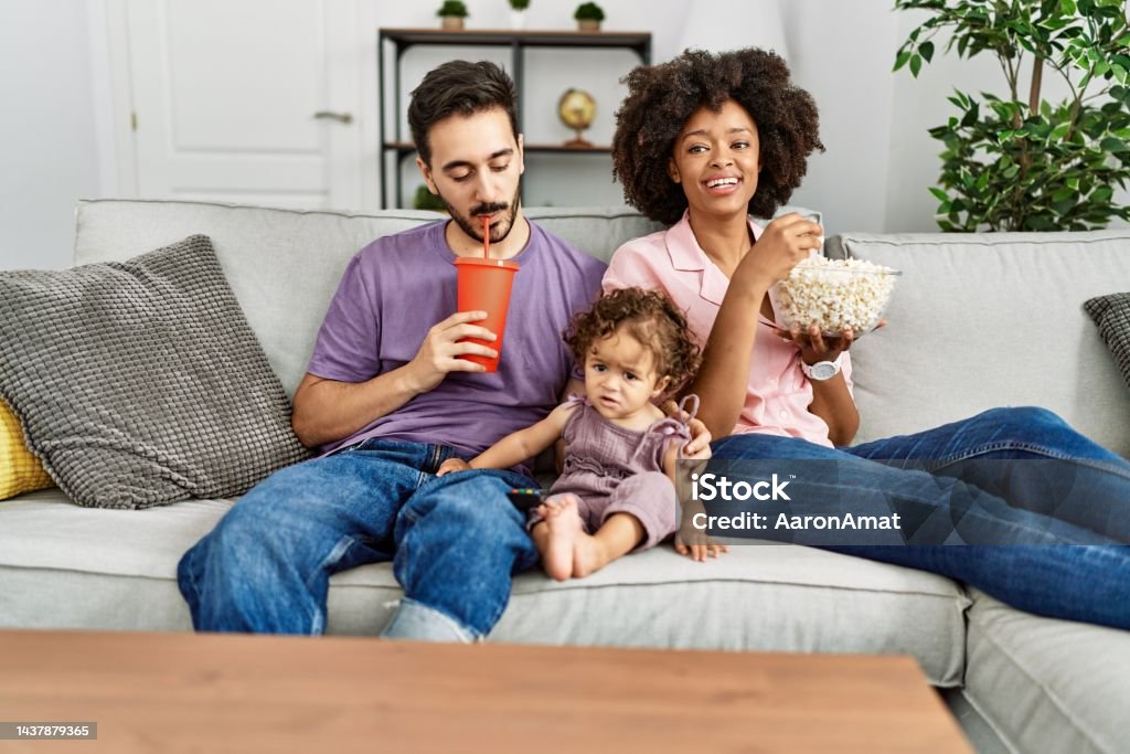 Couple and daughter watching movie sitting on sofa at home Family Stock Photo