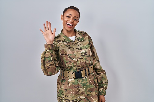 Beautiful african american woman wearing camouflage army uniform waiving saying hello happy and smiling, friendly welcome gesture