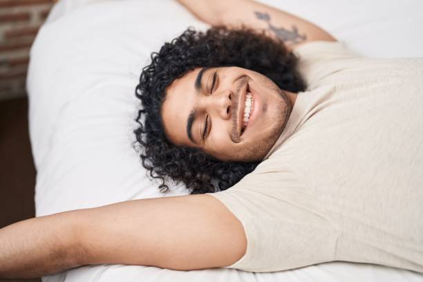 istock Young latin man waking up stretching arms at bedroom 1437879767