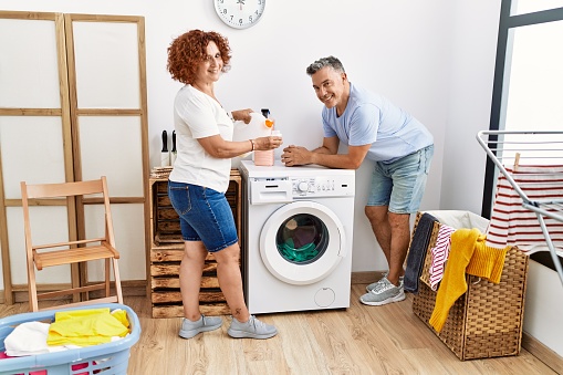 Middle age man and woman couple pouring detergent washing clothes at laundry