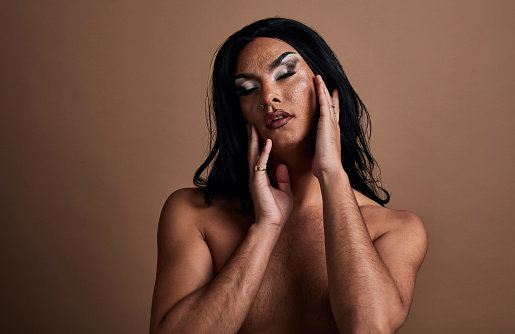 Drag queen, lgbtq and makeup on gay man against brown background for cosmetics, pride and beauty. Male model, glamourous LGBT pride touching face