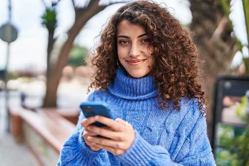 Young hispanic woman smiling confident usng smartphone at street