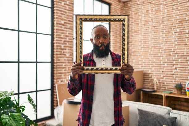 istock African american man putting face in empty frame making fish face with mouth and squinting eyes, crazy and comical. 1437885255