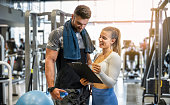 Young female personal trainer showing exercise progress to male client in the gym.