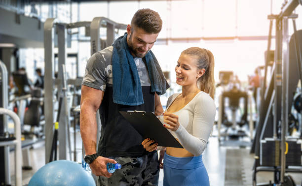 Young female personal trainer showing exercise progress to male client in the gym. Young female personal trainer showing exercise progress to male client in the gym personal trainer stock pictures, royalty-free photos & images