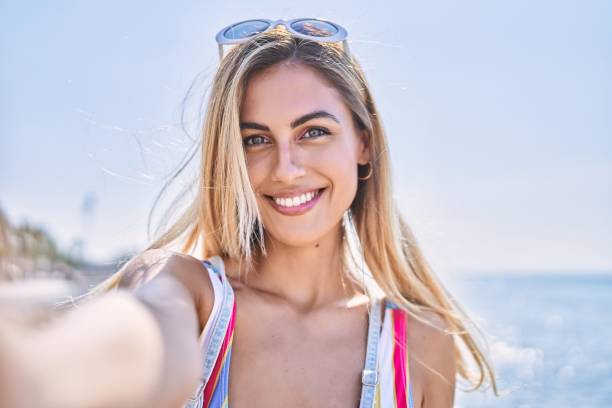 Young blonde girl smiling happy make selfie by the smartphone at the beach. Young blonde girl smiling happy make selfie by the smartphone at the beach. women selfies stock pictures, royalty-free photos & images