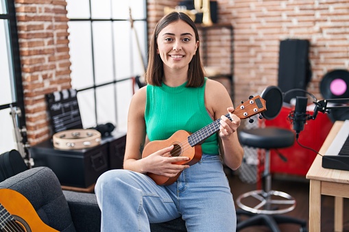 Young hispanic woman musician playing ukelele at music studio