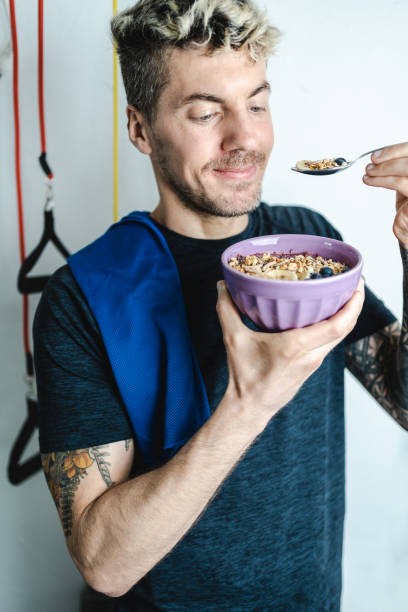 Caucasian tattooed man eating notorious oatmeal bowl after training at home. Fitness and wellbeing concept stock photo