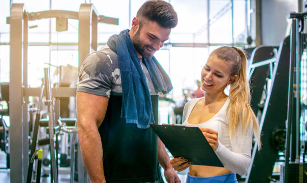 istock Friendly young female personal trainer talking about exercise progress with male client in the gym. 1437888857
