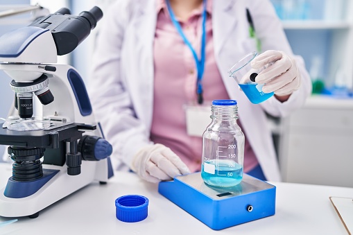 Young beautiful plus size woman scientist pouring liquid on test tube weighing liquid at laboratory