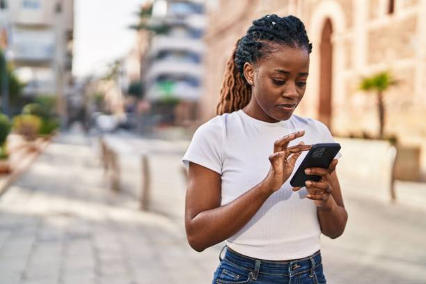 African american woman using smartphone with serious expression at street stock photo