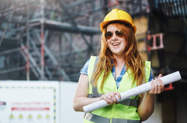istock Happy redhead female construction worker holding building plans and looking proud and contented 1437891279