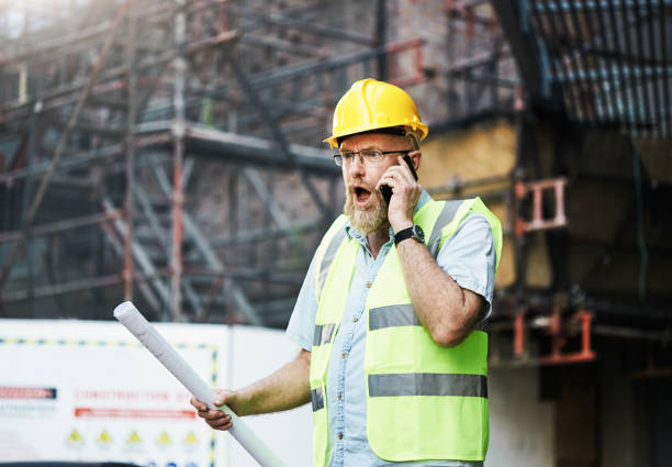 istock Construction worker gets bad news from his mobile phone as he stands on a construction site holding building plans 1437892425