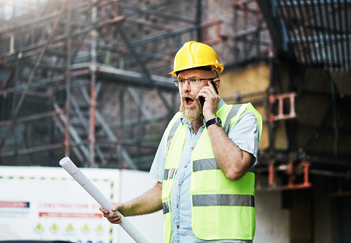 Mature bearded construction guy gasps in horror as he hears bad news on his cellphone.