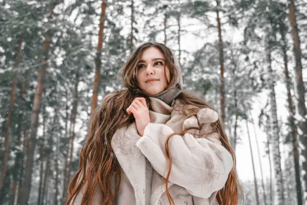 Young beautiful girl in snowy cold winter frost forest. Walking, having fun, laughing in stylish clothes, fur coat, woolen shawl, bonnet. Snow trees lovestory. Romantic date, weekend.