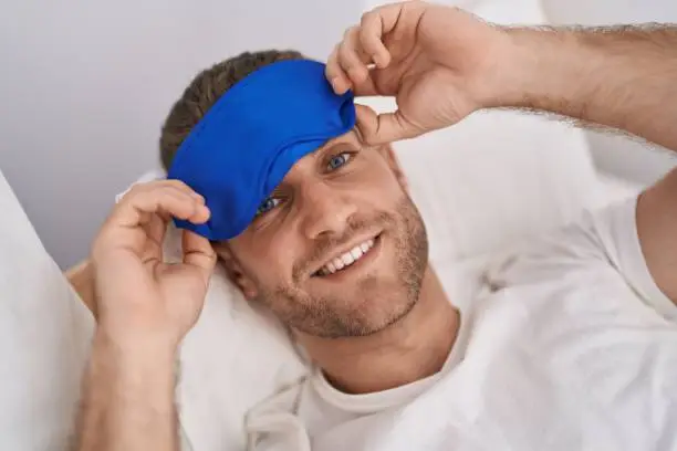 Young caucasian man wearing sleepmask lying on bed at bedroom