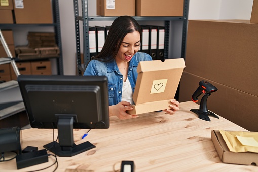Young beautiful hispanic woman ecommerce business worker unboxing package at office