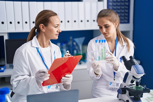 Two women scientists write on document holding test tubes at laboratory