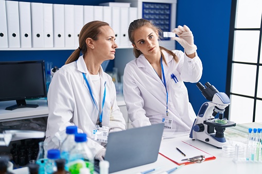 Two women scientists using laptop holding sample at laboratory