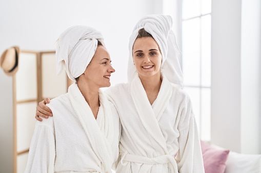 Two women mother and daughter wearing bathrobe hugging each other at bedroom