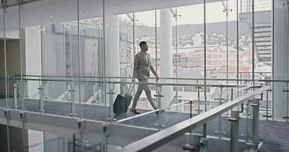 Travel, airport and man walking with luggage at hotel, airport or tradeshow building for success. Male corporate executive on an international business trip for career opportunity with a suitcase