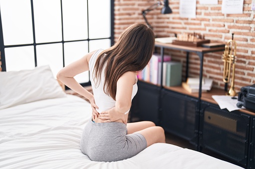 Young caucasian woman suffering for back injury sitting on bed at bedroom