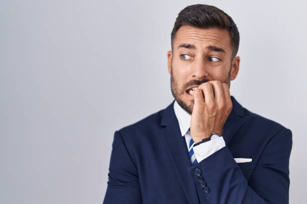 handsome hispanic man wearing suit and tie looking stressed and nervous with hands on mouth biting nails. anxiety problem. - nail biting imagens e fotografias de stock