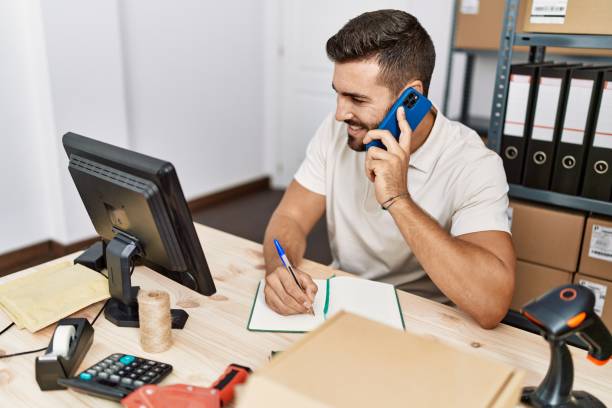 istock Young hispanic man talking on the smartphone writing on notebook at storehouse 1437896639