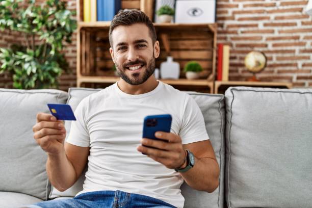 istock Young hispanic man smiling confident using smartphone and credit card at home 1437896643