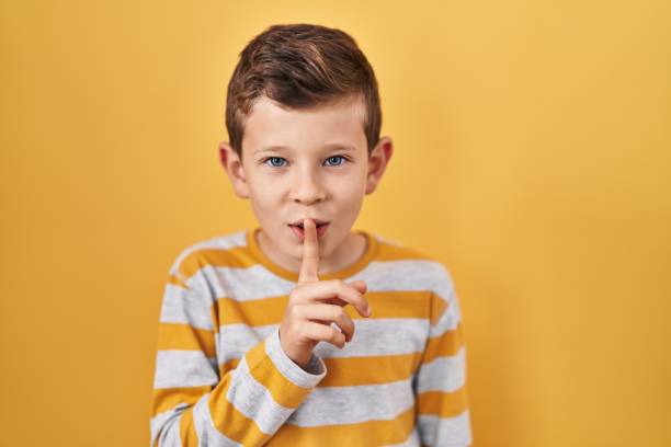Young caucasian kid standing over yellow background asking to be quiet with finger on lips. silence and secret concept.