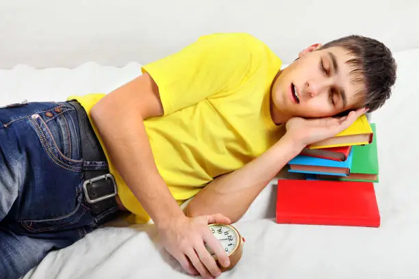 Teenager sleep on the Books with Alarm Clock