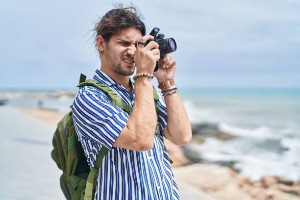 istock Young hispanic man tourist wearing backpack using professional camera at seaside 1437899448